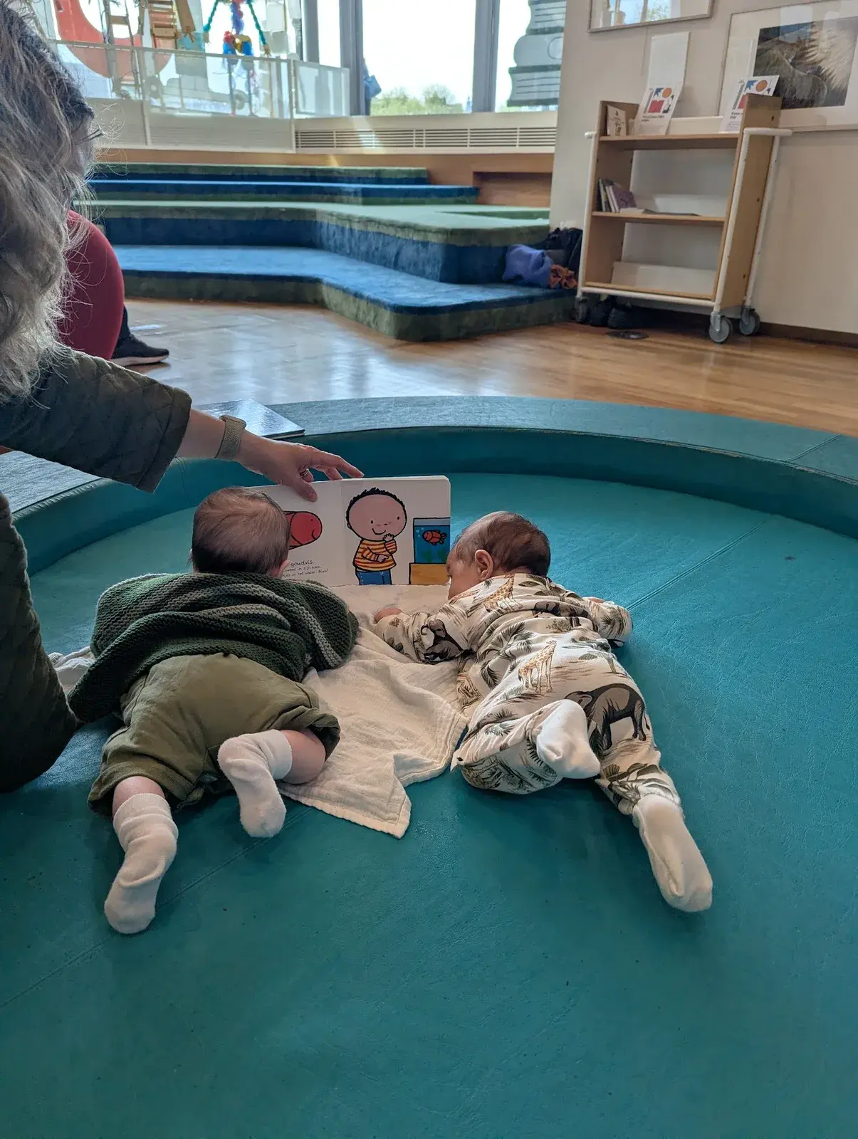 Two babies on their tummies reading a picture book together