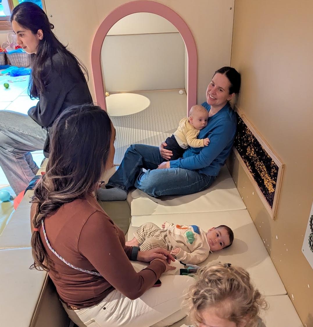 Two parents getting to know each other in a cozy play space, one holding her baby